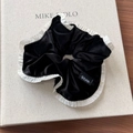 Detail eines schwarzen Samt-Scrunchies mit weißen Plisseekanten auf einem Buch - Schwarzes Pailletten-Haargummi