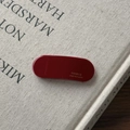 Detailed macro view of smooth oval wine red cellulose acetate clip with gold logo - Red