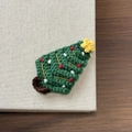 Nahaufnahme einer handgehäkelten Tannenbaum-Haarklammer mit roten und weißen Details - Dunkelgrüner Weihnachtsbaum
