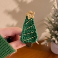 Détail d'une pince à cheveux sapin de Noël au crochet avec textures festives chaudes - Sapin vert avec étoile jaune