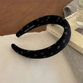 Detail eines Blumen-Schwamm-Stirnbands mit handgefertigtem Etikett auf schwarzem Stoff - Schwarz