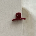 Detail of red acetate hair claw with sparkling colored rhinestones on grey fabric - Red