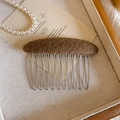 Detail of a brown wool felt hair comb with ten silver metal teeth on a wooden tray - Khaki