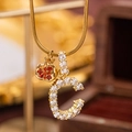 Gold pendant necklace featuring a cubic zirconia letter C and a red garnet-like apple charm - C Style (c)