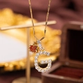 Macro shot of gold letter G pendant with clear zircons and a small red heart charm - Letter G