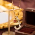 Macro view of gold J letter pendant with white zircons and a small red garnet charm - Letter J