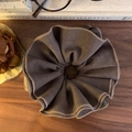 Scrunchie oversize marrone tabacco con trama a pieghe su fondo in legno retro - Marrone