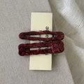 Close-up of a pair of wavy marble wine red acetate hair clips on a display card - Red