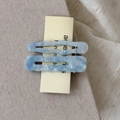 Close-up of blue marble pattern acetate wave hair clips on a soft beige fabric - Blue