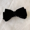 Détail d'une grande pince à cheveux avec nœud en velours noir sur un tissu texturé - Noir