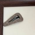 Close-up of triangle wool hair clip with grey-brown felt texture and matte metal base - Apricot