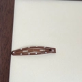 Close-up of brown teardrop-shaped metal hair clip with white polka dots on beige background - Brown