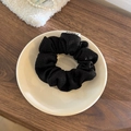 Vue détaillée d'un chouchou en tricot noir avec étiquette sur une assiette en céramique - Petit / Noir