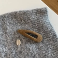 Detailaufnahme der braunen Plüsch-Haarklammer mit silbernem Logo-Tag auf grauem Strick - Hellkaffee Wassertropfen