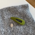 Nahaufnahme einer grünen Strick-Haarklammer mit silbernem Logo auf grauem Wollstoff - Grüner Wassertropfen