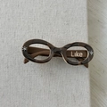 Gros plan d'une pince à cheveux en acétate écaille en forme de lunettes avec motif Like - Marron