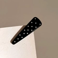 Close-up of a high-gloss triangular hair clip featuring black and white polka dots pattern - Black