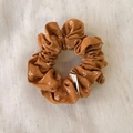 Detailed close-up of brown floral scrunchie on soft linen background with stitched label - Orange Scrunchie