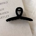 Detail of black flocked hair claw clip featuring non-slip teeth on a beige book - Black