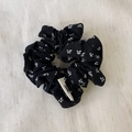 Detailed close-up of a black floral scrunchie featuring white petal patterns and brand tag - Blue Scrunchie