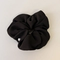 Detail van zwarte stoffen scrunchie textuur met een kleine zilveren merkbedel - Zwart