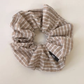 Dettaglio ravvicinato di elastico scrunchie a quadri marroni e beige con logo su sfondo beige - Scrunchie Cachi