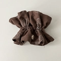 Dettaglio di elastico marrone con stampa paisley, bottone decorativo e tessuto a pieghe - Stile Caffè Sciancrato