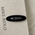 Detalle de una pinza para el pelo ovalada de terciopelo negro sobre fondo beige suave - Ovalado negro