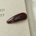 Barrette goutte en cuir PU bordeaux minimaliste avec coutures fines sur un livre - Goutte d'Eau Rouge
