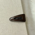 Gros plan d'une barrette en cuir PU marron avec coutures fines sur fond en tissu - Petit Triangle Café