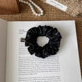 Detail shot of a black vintage PU leather scrunchie on a book with pearl necklace - Black