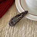 Detailaufnahme der Snap-Haarspange mit Leopardenmuster auf Keramik und Strickhintergrund - Wassertropfen Kaffee Leopardenmuster