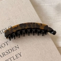 Close-up of a leopard print banana hair clip with multi-tooth grip on a book - Tortoise