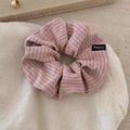 Close-up of a striped hair scrunchie with a logo label on soft beige knit fabric - Pink