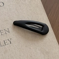 Dettaglio di un fermaglio BB in ecopelle nera su una superficie di un libro materico - Goccia d'acqua Nero