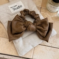 Dettaglio dell'elastico per capelli in pelle marrone scuro con fiocco su sacchetto di iuta - Marrone