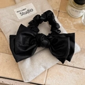 Close-up of black leather bow hair tie with textured finish on a rustic linen pouch - Black