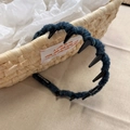 Close-up of a blue knitted headband with inner teeth and a handmade label on a basket - Wavy Headband / Blue