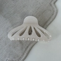 Close-up of cream fan-shaped hair claw with hollow design on textured grey linen - White
