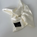 Detailopname van de crème satijnen scrunchie met fijne stoftextuur en handgemaakt label - Melkwit