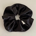 Detail van zwarte satijnen scrunchie met handgemaakt label en gladde glanzende textuur - Zwart