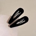 Detailed macro view of two black velvet-textured teardrop BB hair clips on beige backdrop - Black