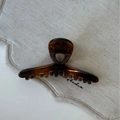 Détail de la pince à cheveux écaille ambrée sur tissu beige montrant la texture brillante - Écaille de tortue