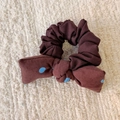 Dettaglio scrunchie marrone con fiocco a pois blu su sfondo a trama morbida - Elastico con fiocco