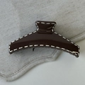 Detail of a dark brown glossy hair claw clip with white stitching on gray linen - Coffee Bar