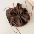 Detail of coffee brown scrunchie with striped fabric texture and small bow ties - Brown