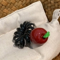 Detalle de colgante de manzana roja en goma de pelo espiral negra y clara en una cesta - Manzana