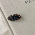 Détail macro d'une pince à cheveux ovale en acétate avec strass colorés sur un livre - Dégradé bleu marron