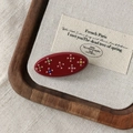 Detailed macro view of an oval red acetate hair clip featuring colorful rhinestone flowers - Red