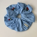 Dettaglio di uno scrunchie in denim azzurro con ricamo a ciliegia e etichetta Happiness - Elastico per capelli / Scrunchie Blu Chiaro